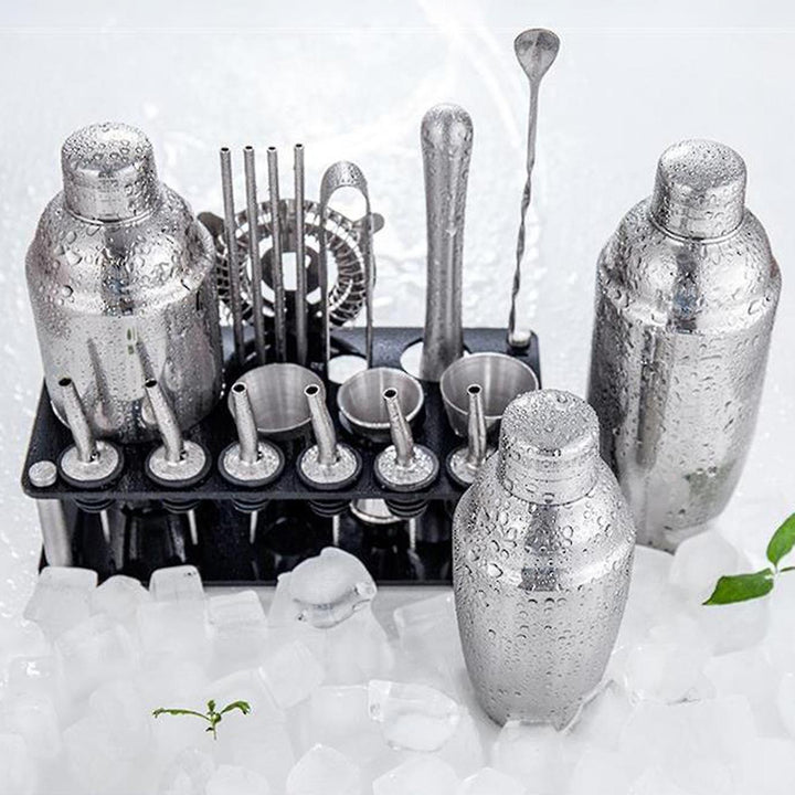 Komplet bartender-kit i rustfrit stål med alle nødvendige redskaber som martini-shaker og jigger, præsenteret på en bambusstander.