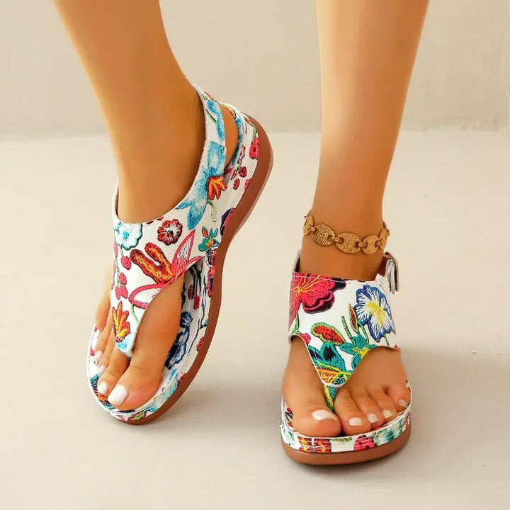 Elegant sort/hvid blomstret dame ortopædisk kilehæl sandal. Justerbar for komfort og stil til sommerbrug.
