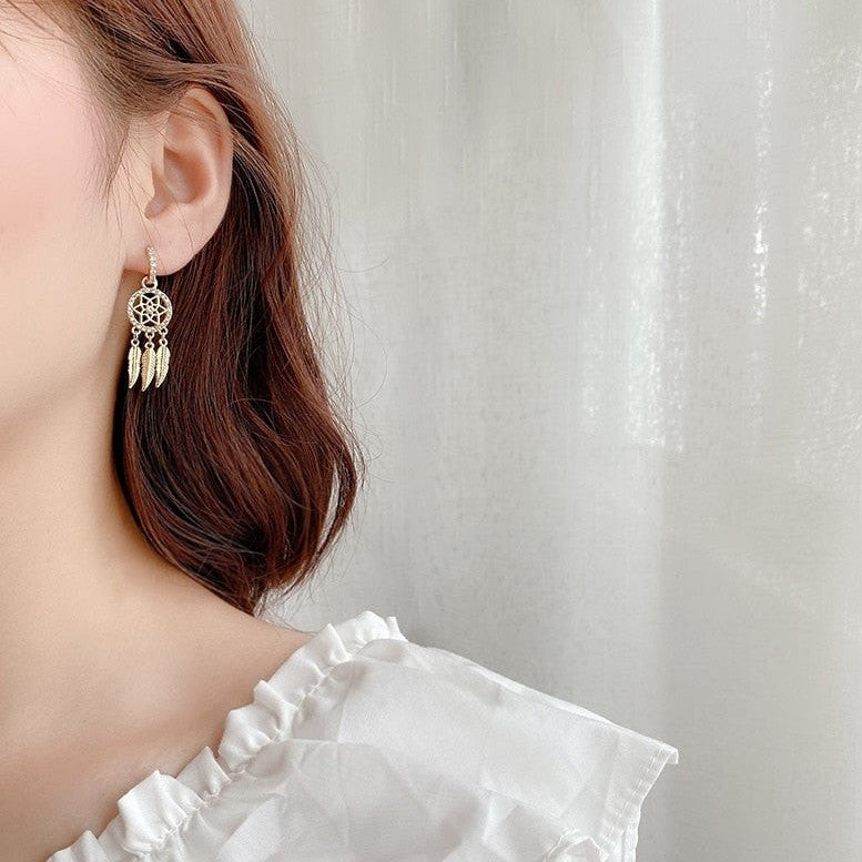 Nærbillede af 14 karat guld drømmefangerøreringe. Detaljer med fjer, indfattede krystaller for et elegant look.