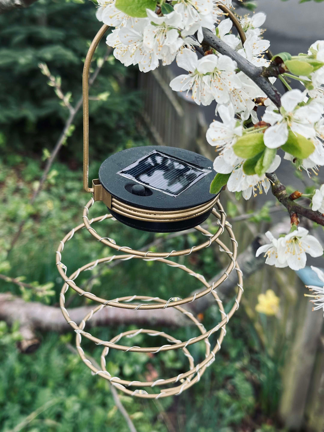 Gylden solcelle spiral lampe lyser op i haven om aftenen. Skaber en varm og indbydende stemning med LED udendørslys.