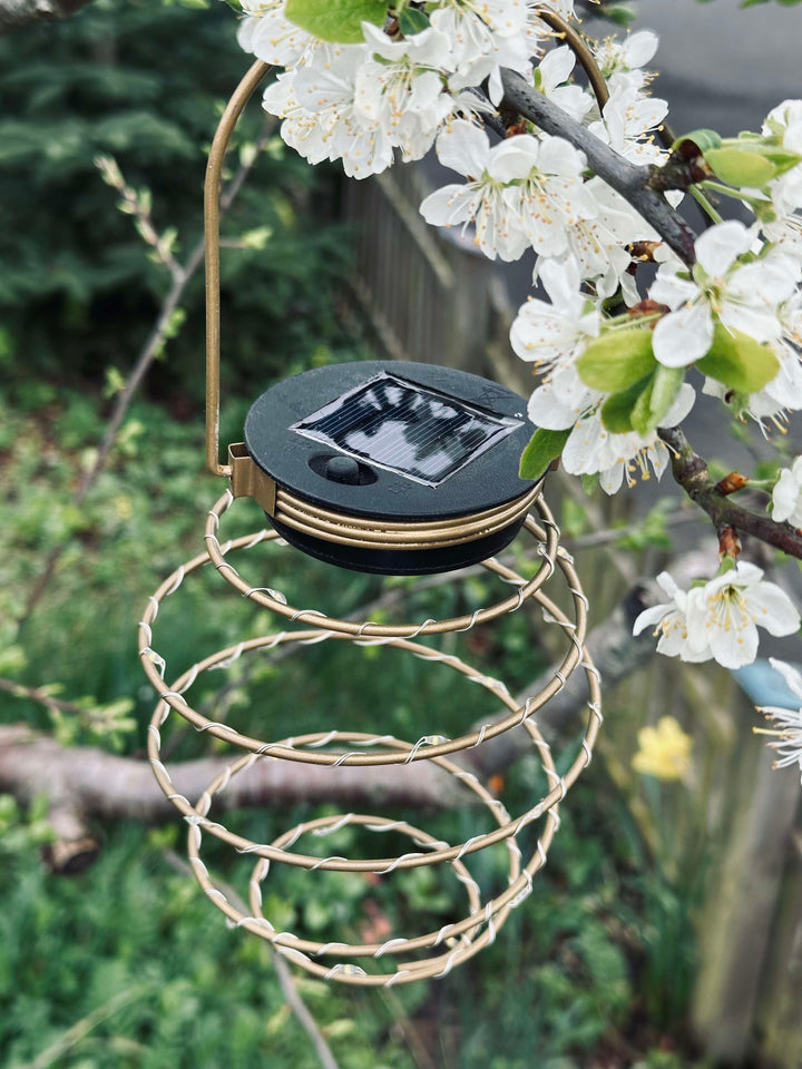 Gylden solcelle spiral lampe lyser op i haven om aftenen. Skaber en varm og indbydende stemning med LED udendørslys.