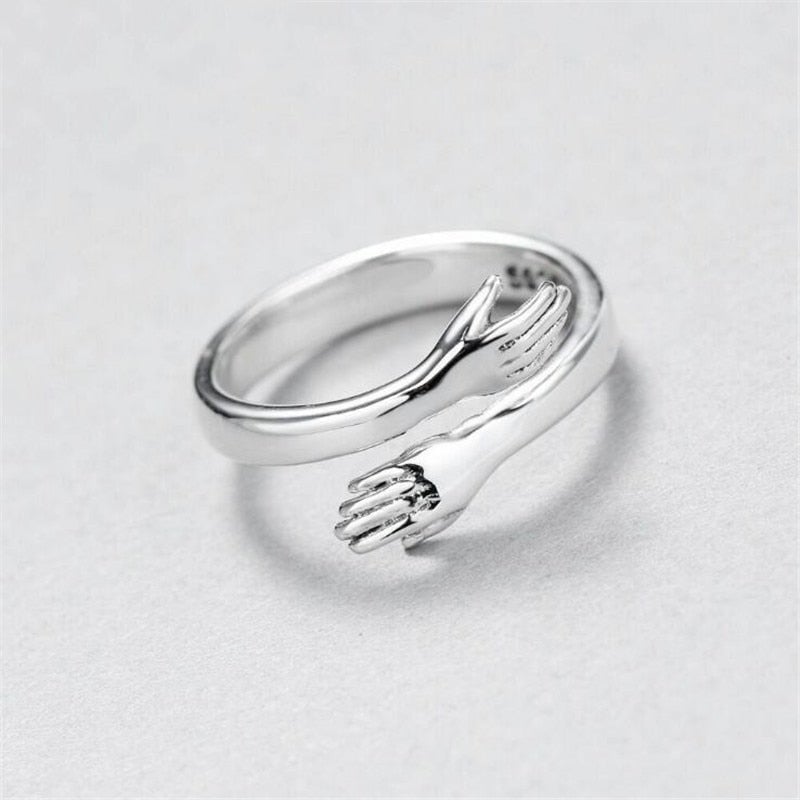 Detaljeret billede af en glat sølvfarvet krammering, der omfavner fingeren. En justerbar kærlighedsring med dyb symbolik.