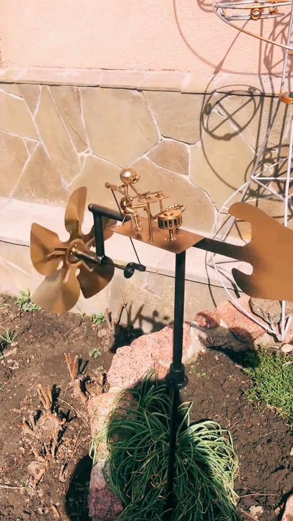 Smuk metal vindmølle der fanger vinden, tilføjer dynamisk havekunst og havedesign.