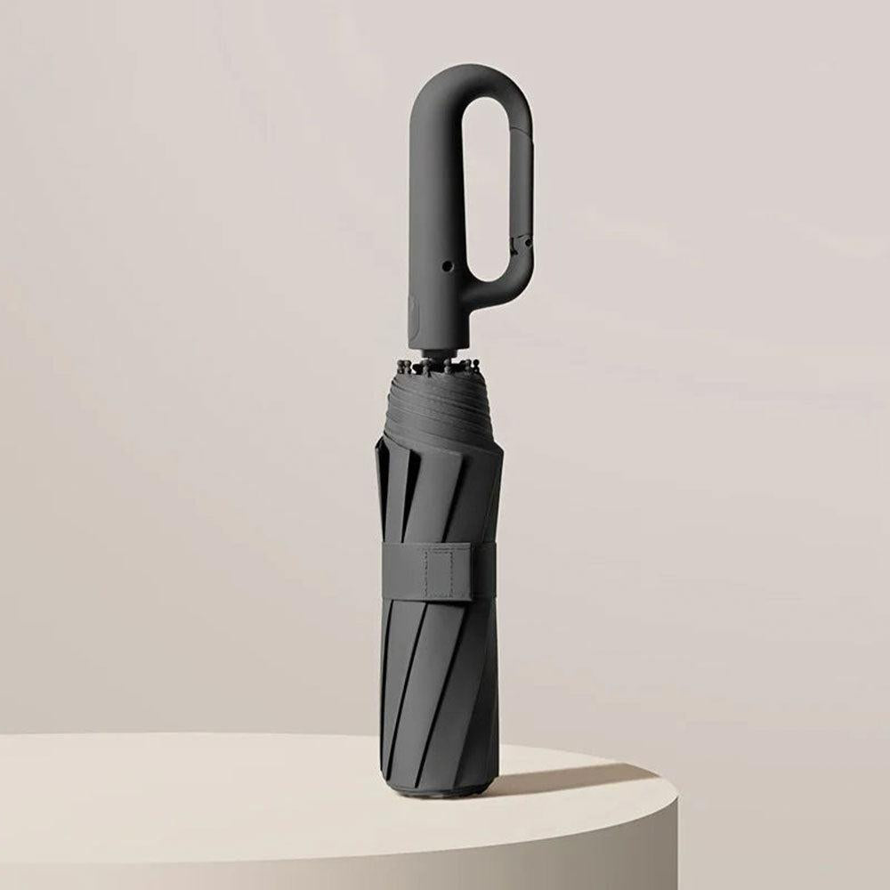 Kompakt sort rejseparaply med UV-beskyttelse, foldet og klar til tasken. Ideel til alle vejrforhold.