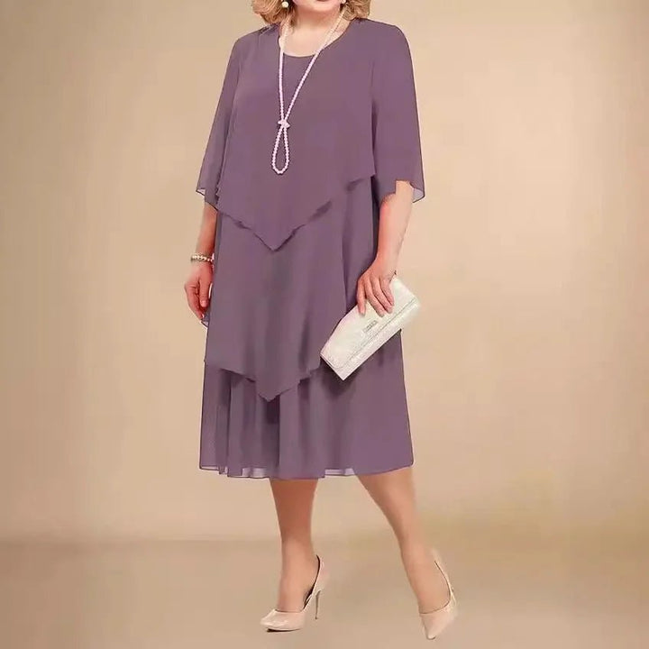 Lilla plus size festkjole i chiffon med elegant asymmetrisk design. Knælang damekjole til selskab.