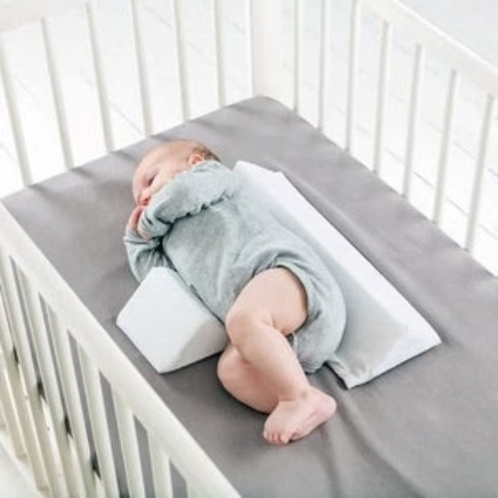 Justerbar baby anti-rulle kilepude, hvid, med burrelukninger; understøtter sikker søvn og forhindrer rulning.