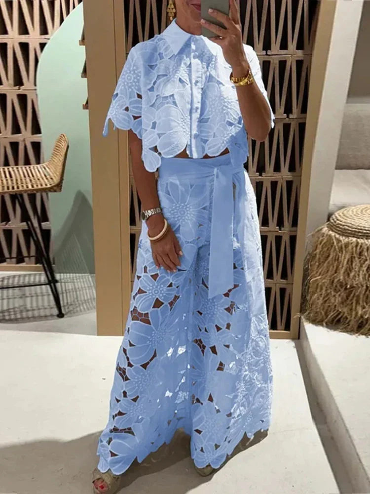 Model iført et stilfuldt blomstret blondesæt med crop top og brede bukser, perfekt til sommer.